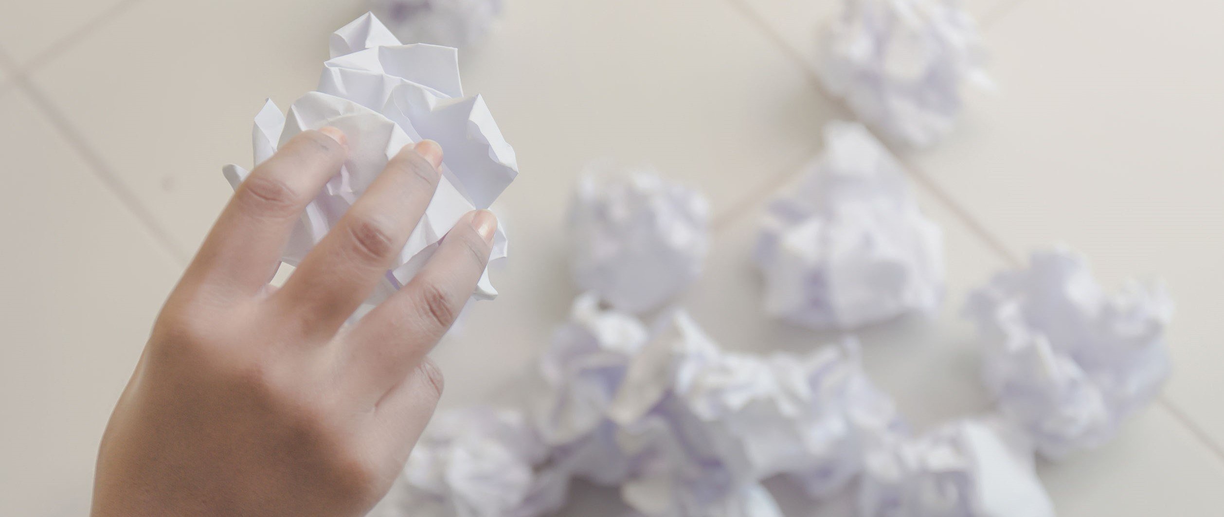 Human hand holding crumpled paper or trash and white paper ball and waste on the floor, A hand are crumpling a paper