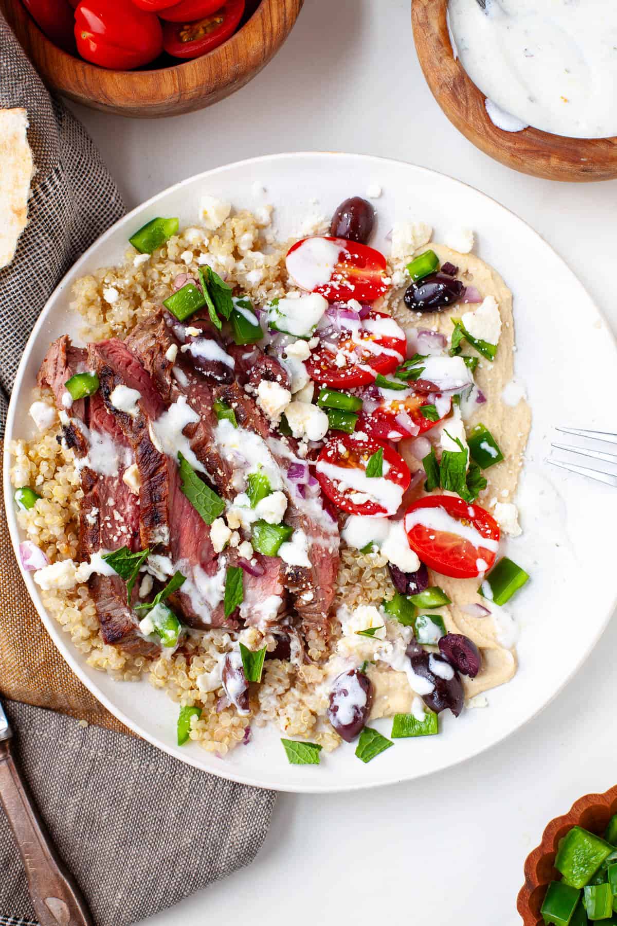 steak grain bowl with cherry tomatoes, quinoa, bell pepper, olives, feta, hummus, mint, and yogurt dressing